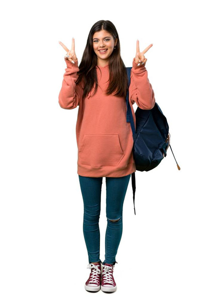 Una foto completa de una adolescente con sudadera y mochila sonriendo y mostrando el signo de victoria con ambas manos
 - Foto, Imagen