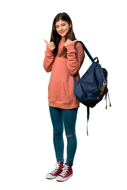 Una foto completa de una adolescente con sudadera y mochila dando un gesto de pulgares hacia arriba con ambas manos y sonriendo
 - Foto, Imagen