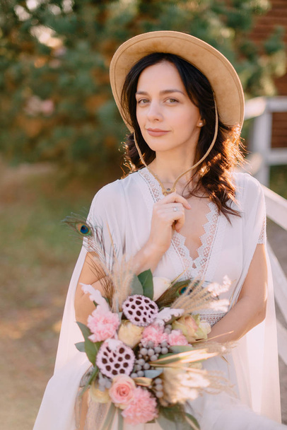 young boho-style bride standing near fence holding bouquet - Foto, immagini