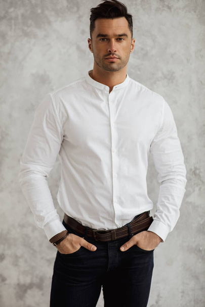 Handsome man in white shirt with hands in pockets looking at camera - Valokuva, kuva