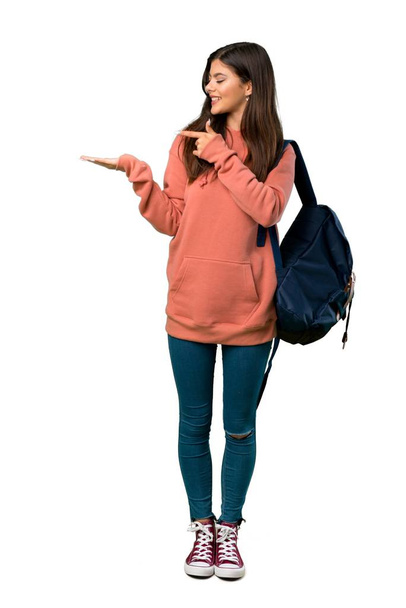 A full-length shot of a Teenager girl with sweatshirt and backpack holding copyspace imaginary on the palm to insert an ad - Photo, Image
