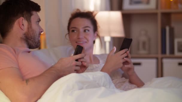 happy couple using smartphones in bed at night - Filmagem, Vídeo