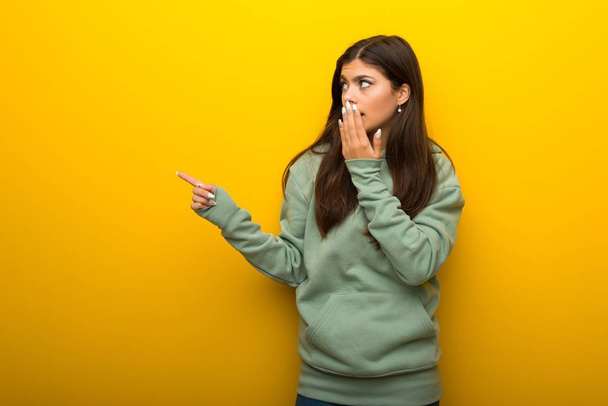 Teenager Mädchen mit grünem Sweatshirt auf gelbem Hintergrund zeigt mit dem Finger zur Seite mit einem überraschten Gesicht - Foto, Bild