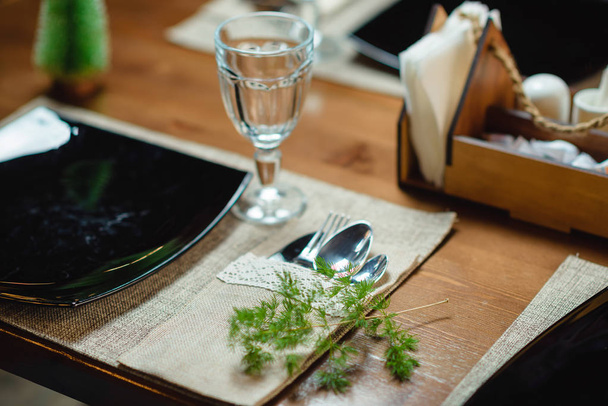 Festive table setting. Cutlery. Wooden table. Glass glasses. Table decor plants. Spruce twig. Cloth napkins for the table. A plate of black color. - Фото, зображення
