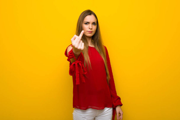 Young girl with red dress over yellow wall making horn gesture - Fotó, kép