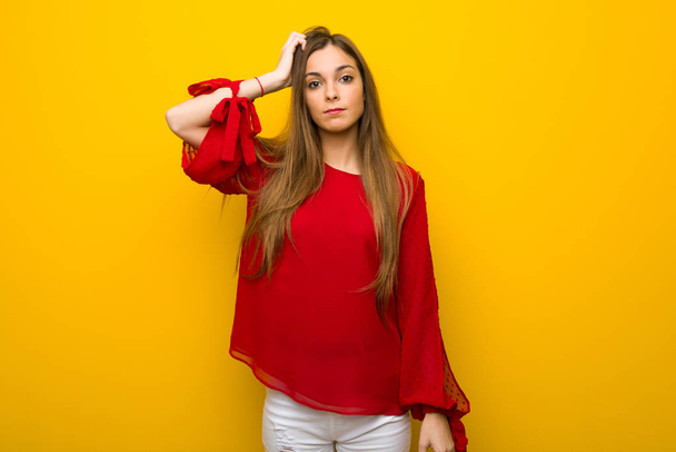 Jovem com vestido vermelho sobre a parede amarela com uma expressão de frustração e não compreensão
 - Foto, Imagem