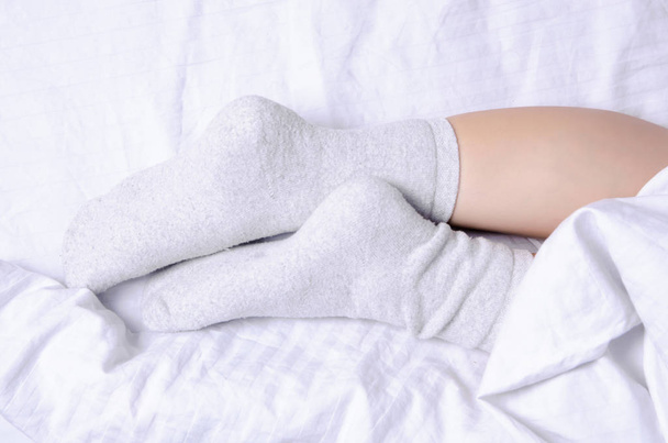 Female legs in white gray socks in white linens bed - Foto, Imagen