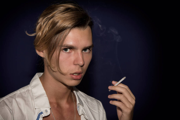 A young guy smokes a cigarette. Bad habits. Dark background. - Photo, Image