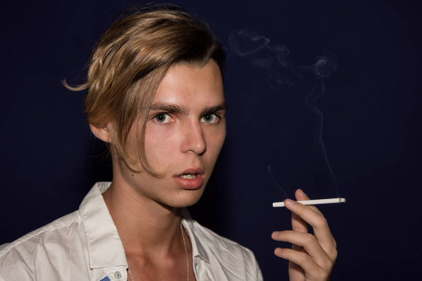 A young guy smokes a cigarette. Bad habits. Dark background. - Photo, Image