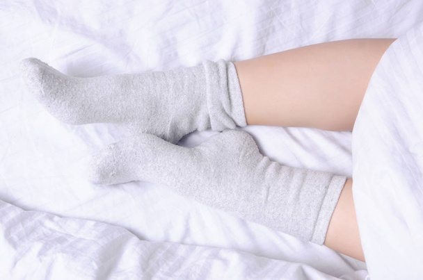 Female legs in white gray socks in white linens bed - Foto, afbeelding