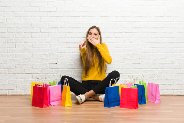 Fiatal lány sok bevásárló táskák valaki ujjal mutatva, és nevetve - Fotó, kép