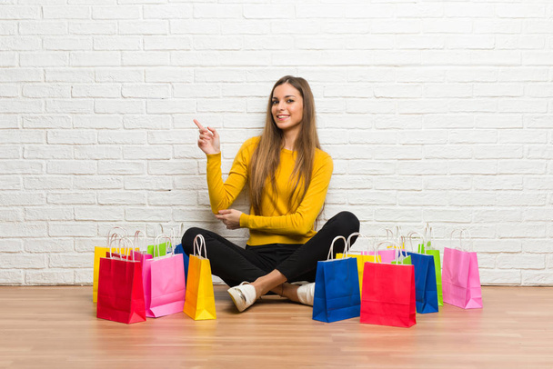 Young girl with lot of shopping bags pointing finger to the side in lateral position - Photo, Image