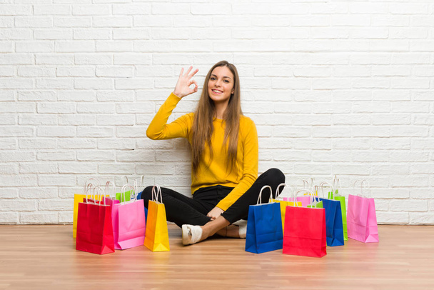 Menina com muitos sacos de compras mostrando um sinal ok com os dedos
 - Foto, Imagem