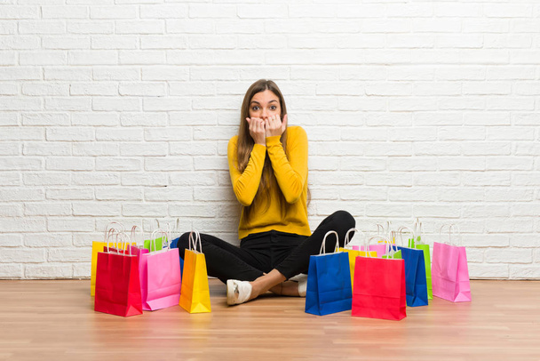 Young girl with lot of shopping bags is a little bit nervous and scared putting hands to mouth - Photo, Image