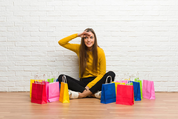 Mladá dívka s množstvím nákupních tašek pohledu daleko rukou dávat něco - Fotografie, Obrázek
