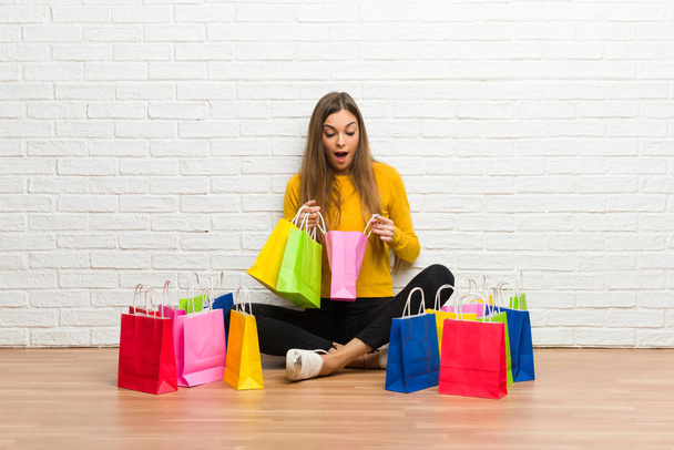 Chica joven con un montón de bolsas de compras sorprendido mientras sostiene una gran cantidad de bolsas de compras - Foto, imagen