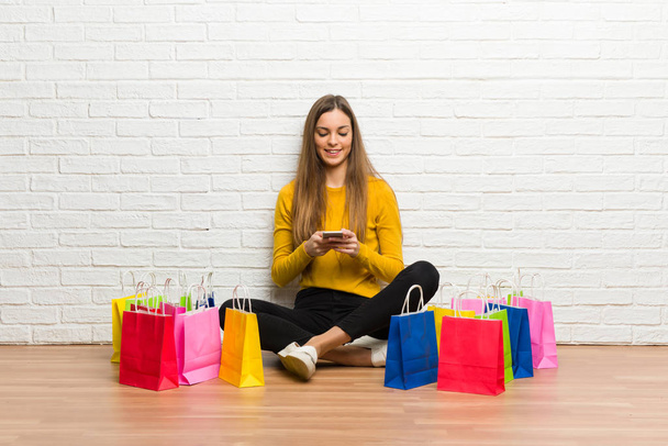 Chica joven con un montón de bolsas de compras enviando un mensaje con el móvil
 - Foto, imagen
