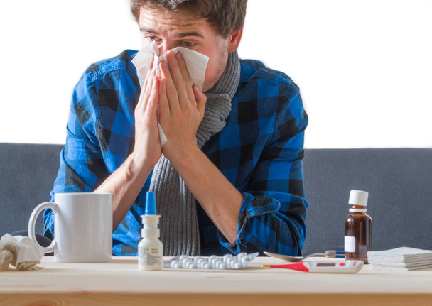 Joven hombre caucásico con camisa azul está teniendo un resfriado, estornudando en un pañuelo
 - Foto, imagen