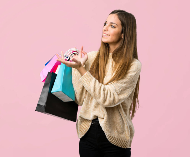 Fiatal lány bevásárló táskák, kiterjesztve a kezét, hogy az oldalon meghívó eljövendő izolált rózsaszín háttér - Fotó, kép