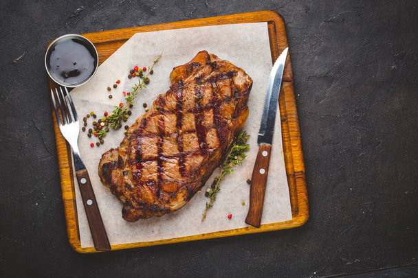 Succulent steak striploïne grillé garni d'herbes et de sel. Avec fourchette et couteau à côté sur planche à découper
 - Photo, image