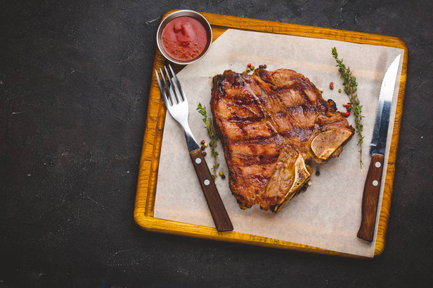 Succulent grillé gros t-bone steak garni d'herbes et de sel. Avec fourchette et couteau à côté sur planche à découper
  - Photo, image