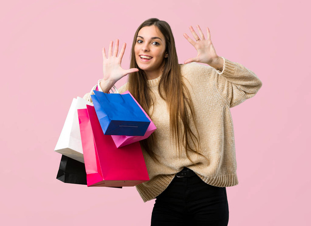 Young girl with shopping bags counting ten with fingers on isolated pink background - Fotó, kép