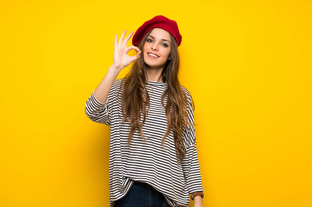 Mädchen mit französischem Stil über gelbe Wand zeigt ein ok Zeichen mit Fingern - Foto, Bild