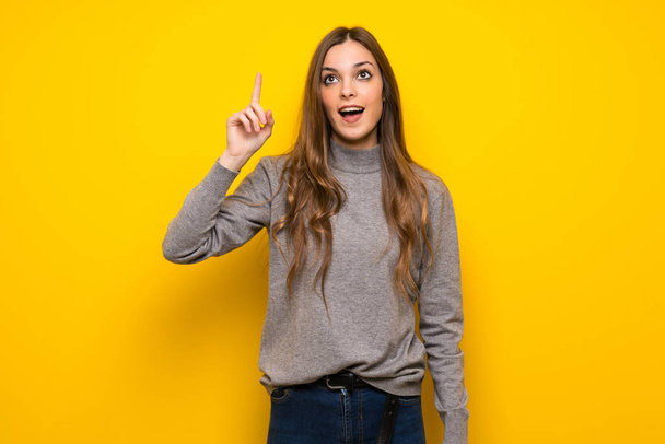 黄色の壁にしようとする以上の若い女性が指を持ち上げながらソリューションを実現します。 - 写真・画像
