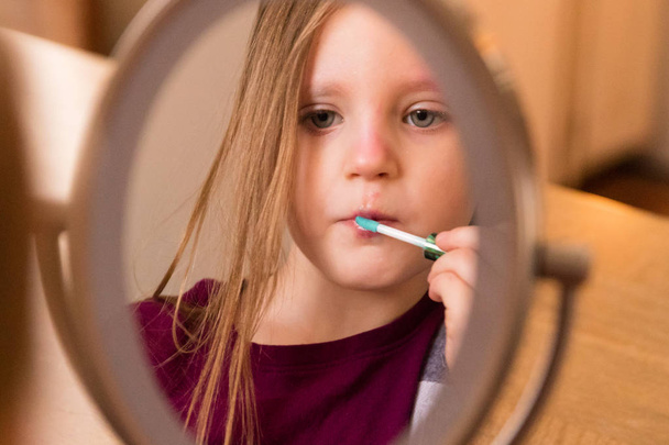 Un niño de 3 años mirándose en el espejo y maquillándose
. - Foto, Imagen