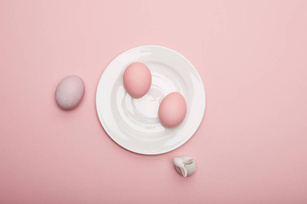 Προβολή επάνω παιχνίδι λαγουδάκι, βαμμένα αυγά του Πάσχα στο πιάτο σε ροζ φόντο - Φωτογραφία, εικόνα