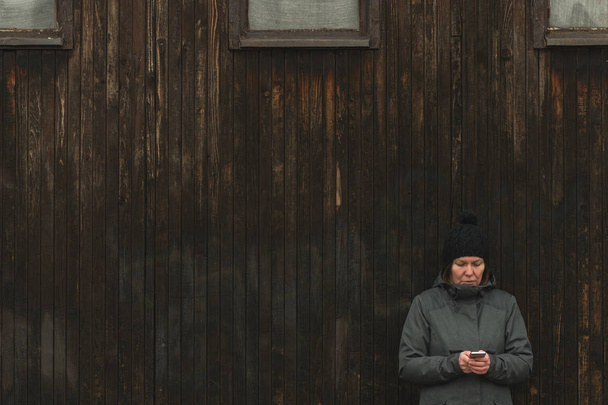 Serious casual female is texting message on mobile phone on street in cold winter afternoon - Fotografie, Obrázek