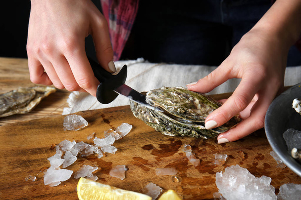 Woman opening raw oyster with knife at table, closeup - Valokuva, kuva