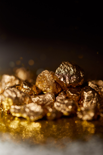 foco seletivo de pedras douradas na superfície espumante escura e fundo preto
 - Foto, Imagem