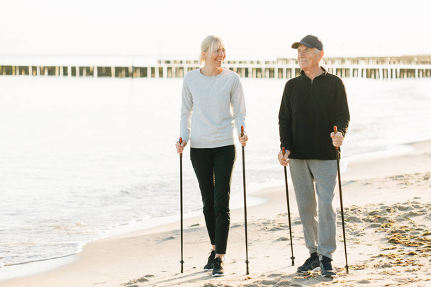 Nordic walking - senior man and pretty young girl working out on beach. Healthy lifestyle. Candid photo of father and daughter. - Photo, Image