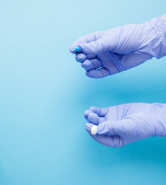 Woman hands in medical gloves giving two big pills. Blue and white. Make your selection. Copy space. - Foto, afbeelding