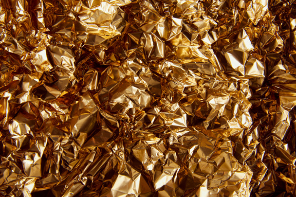 top view of crumpled golden foil with glares - Foto, afbeelding