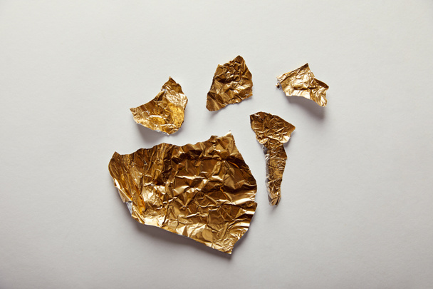 top view of pieces golden foil with glares on white background - Foto, immagini