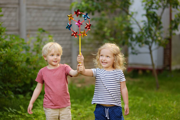 Little boy and girl having fun during walk. Happy child with pinwheel. Preschoolers or toddlers birthday party in summer park. - Foto, imagen