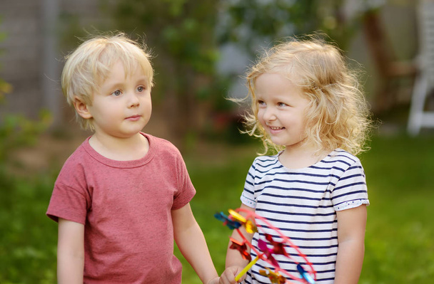 Little boy and girl having fun during walk. Happy kids with pinwheel. Preschoolers or toddlers birthday party in summer park. - Photo, Image