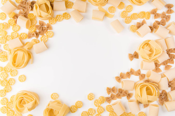 An overhead photo of different types of pasta, including spaghetti, penne, fusilli, and others, flay lay on a white background with a place for text - Foto, Imagen