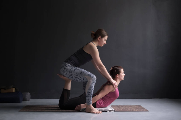 Sporty yoga girl help her friend to do bhudjangasana or Cobra Pose - Foto, afbeelding