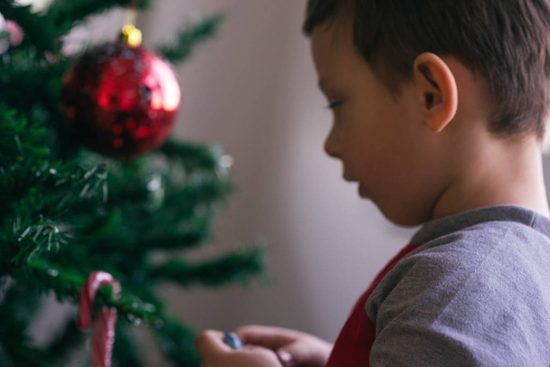 Cute kid is decorating his family Christmas tree while spreading the Christmas spirit in his family. - Φωτογραφία, εικόνα