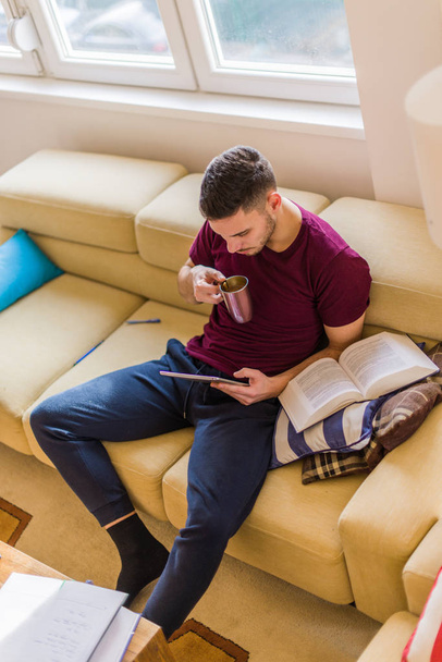 Young man is drinking coffee and looking at his tablet - Photo, Image