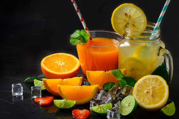 Pomerančové a citrónové šťávy s čerstvým plátek pomeranče a plátek citron na černém pozadí kamene, letní nápoje koncepce - Fotografie, Obrázek
