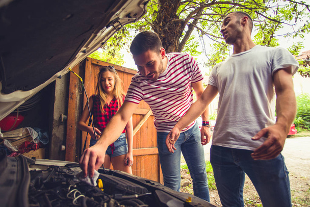Guy looking worried fixing car problem with a girl and man next to him - Photo, Image