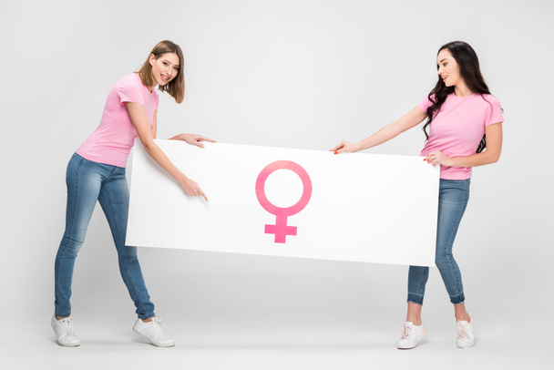 cheerful woman pointing with finger at large sign with female symbol near girl on grey background - Photo, Image
