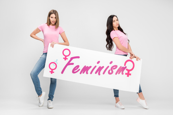 attraktive Frauen mit großem Schild mit Feminismus-Schriftzug auf grauem Hintergrund - Foto, Bild