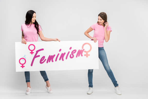 wesoły kobiet posiadających duży znak z napisem feminizmu na szarym tle - Zdjęcie, obraz