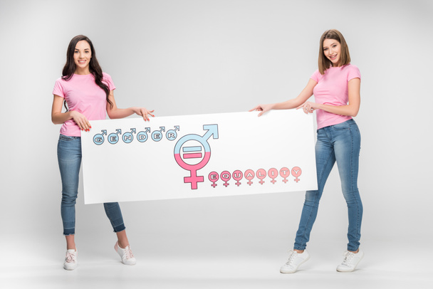 mujeres hermosas sosteniendo letrero grande con símbolo de igualdad de género sobre fondo gris
 - Foto, Imagen