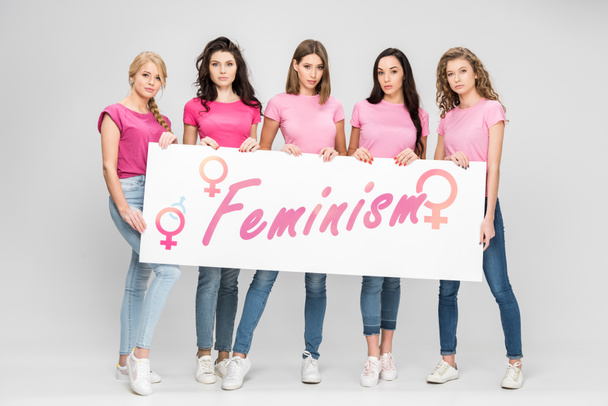 attractive girls holding large sign with feminism lettering on grey background - Fotó, kép